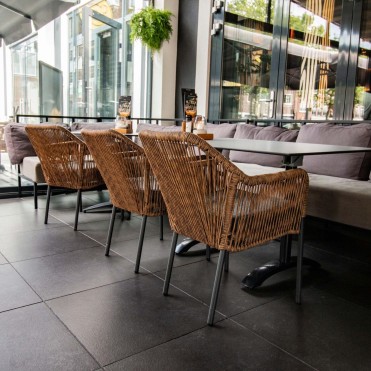 Natūralios spalvos „Baleric“ terasos kėdžių komplektas, moderniai išdėstytas restorane, su antracito spalvos aliuminio rėmais ir tamsiai pilkomis pagalvėlėmis.