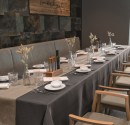 Long restaurant table with dark grey tablecloth, beige table runner and white napkins
