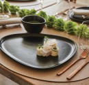 A black plate with food on it, placed on an oval brown placemat.