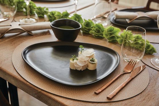 A black plate with food on it, placed on an oval brown placemat.