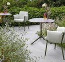 A lush outdoor terrace with light green chairs and tables, surrounded by vibrant greenery and flowers, creating a serene dining atmosphere.